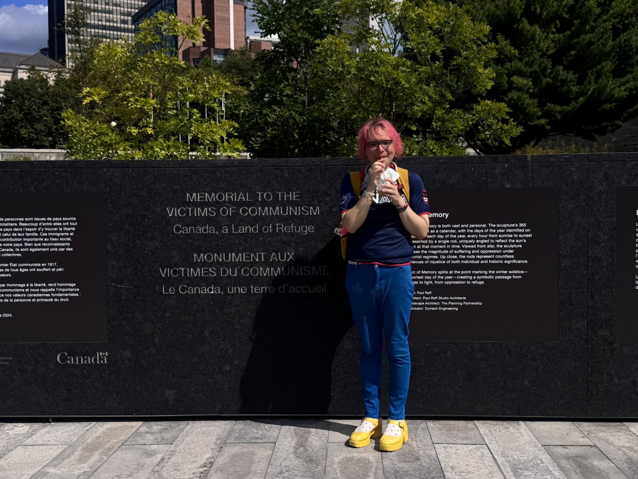 chee rabbits standing in front of the victims of communism memorial, slightly smiling, sipping an iced latte