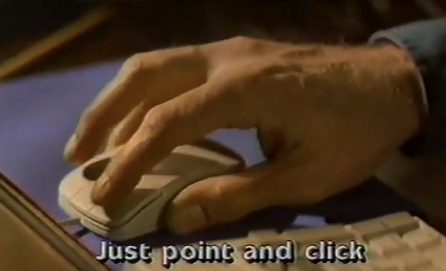 a human hand operating a computer mouse with the caption 'just point and click'. looks like a frame from a VHS video