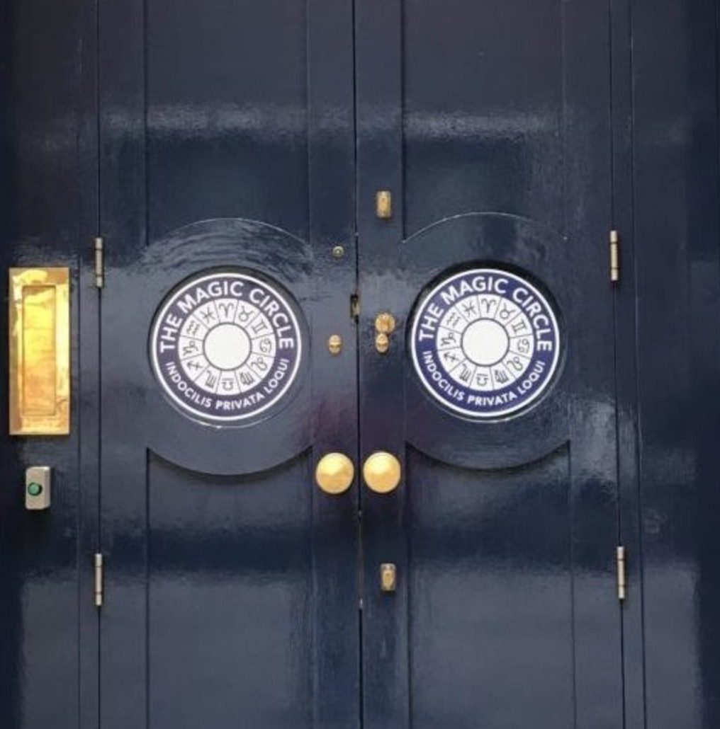 blue and gold door with circular logo "the magic ✨ circle indocillis privata
loqui" and the astrological signs around an empty white
circle
