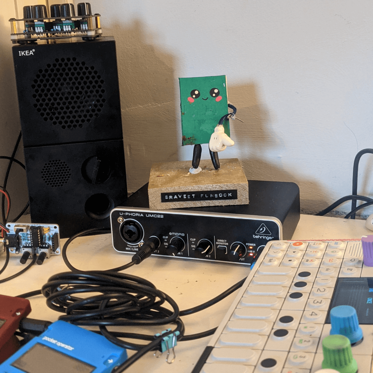 a beat-up green runbook figurine stands on top of an audio interface, looking
out over some teenage engineering synths. it is making a groovy sideways thumb
gesture with its remaining arm
